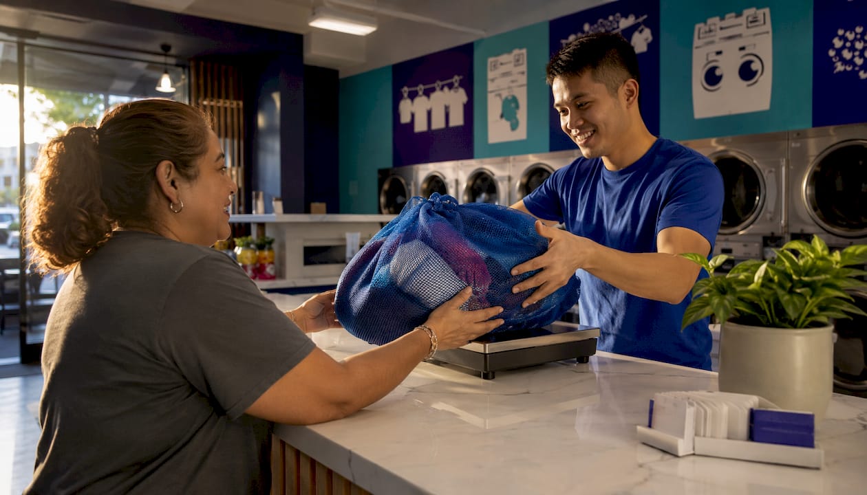 Customer handing laundry bag to attendant at laundromat