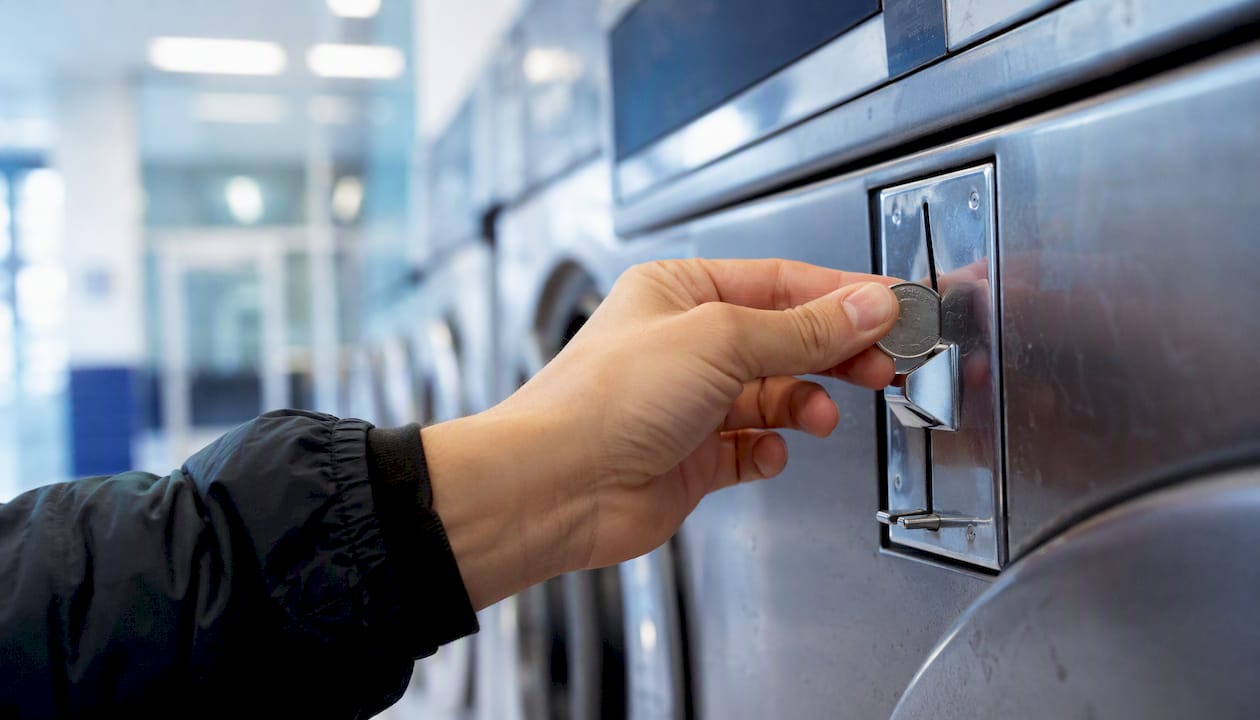Hand inserting quarters into laundry machine coin slot